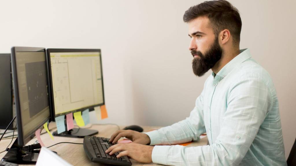 Focused man using dual monitors to design content layouts, showing content creation workflow for growth hacks for content marketing.