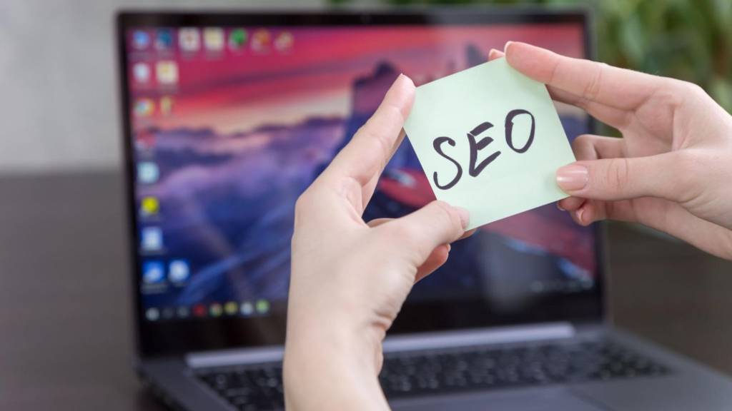 Sticky note labeled SEO in front of a laptop used for AI search strategy