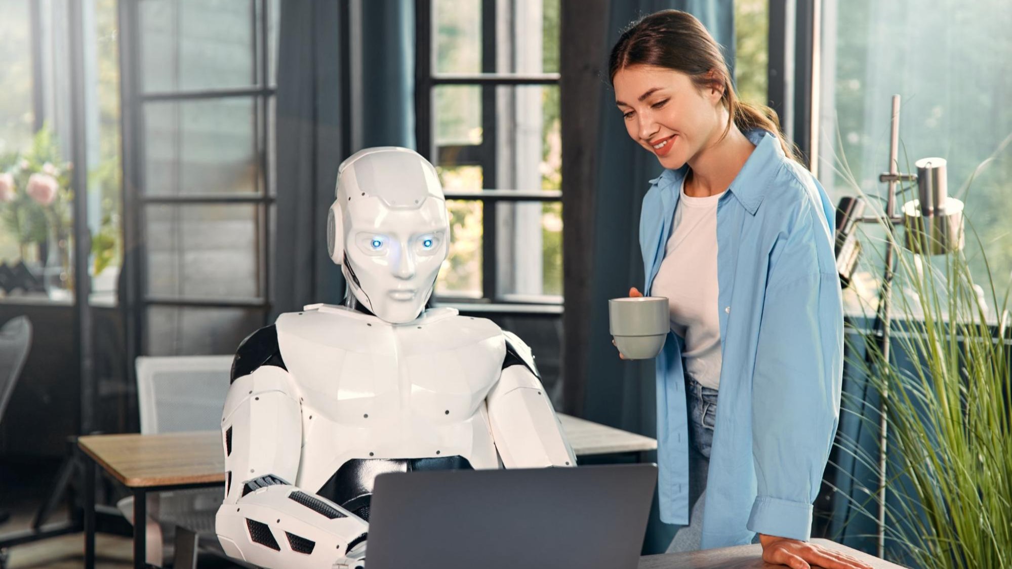 A woman collaborating with a humanoid robot on a laptop, symbolizing how AI supports rather than replaces human creativity in digital marketing.