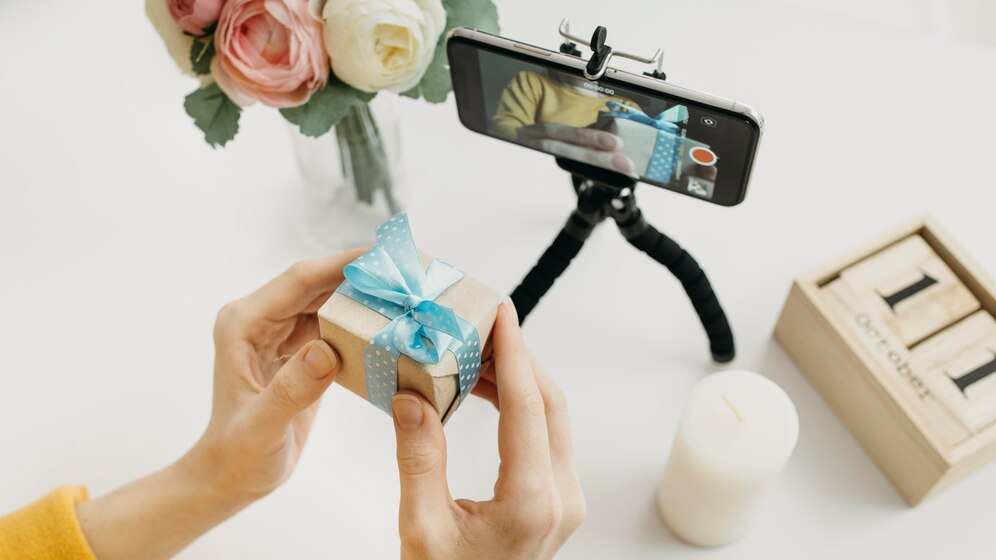 Woman using her phone and a gift box to create social media content for her e-commerce website jewerly store