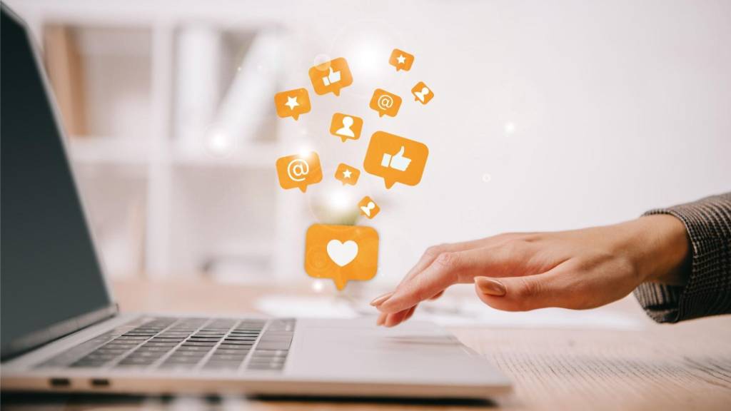Social media engagement icons above laptop representing cross-platform ads and digital marketing within a unified ad strategy.