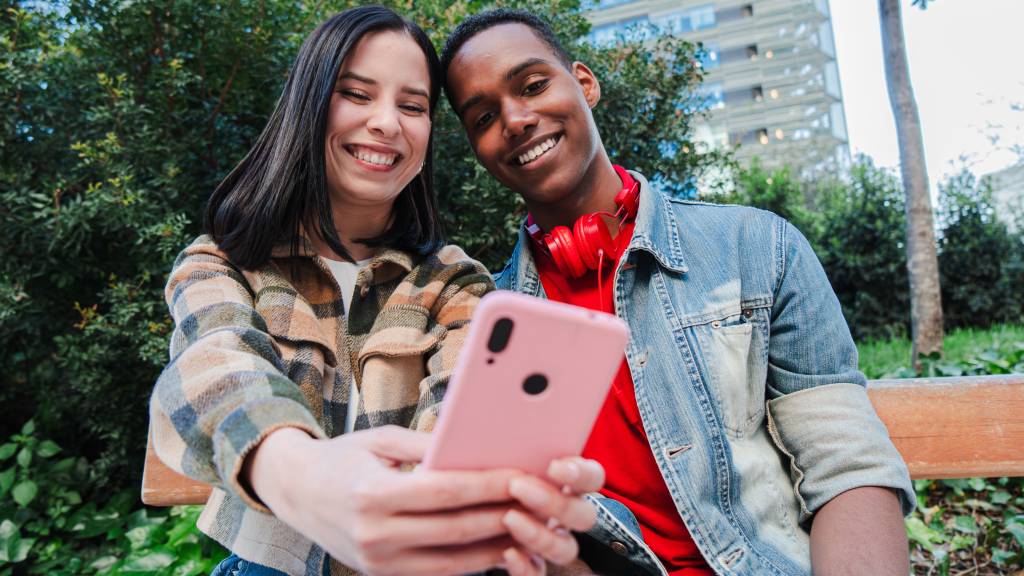 Smiling young friends taking a selfie together in a park for TikTok content in Latin America.