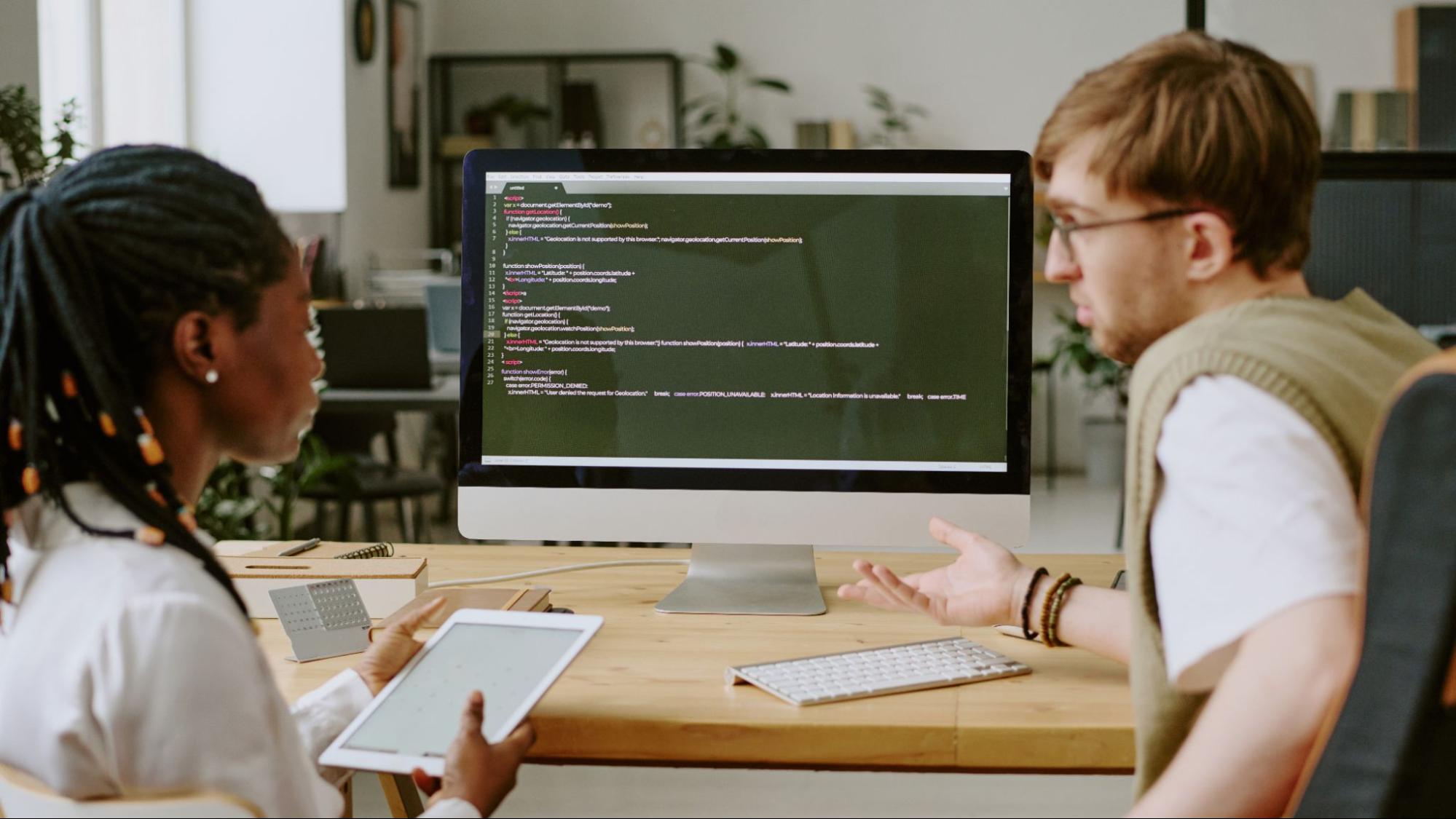 Two developers reviewing website code and discussing SEO-friendly solutions.
