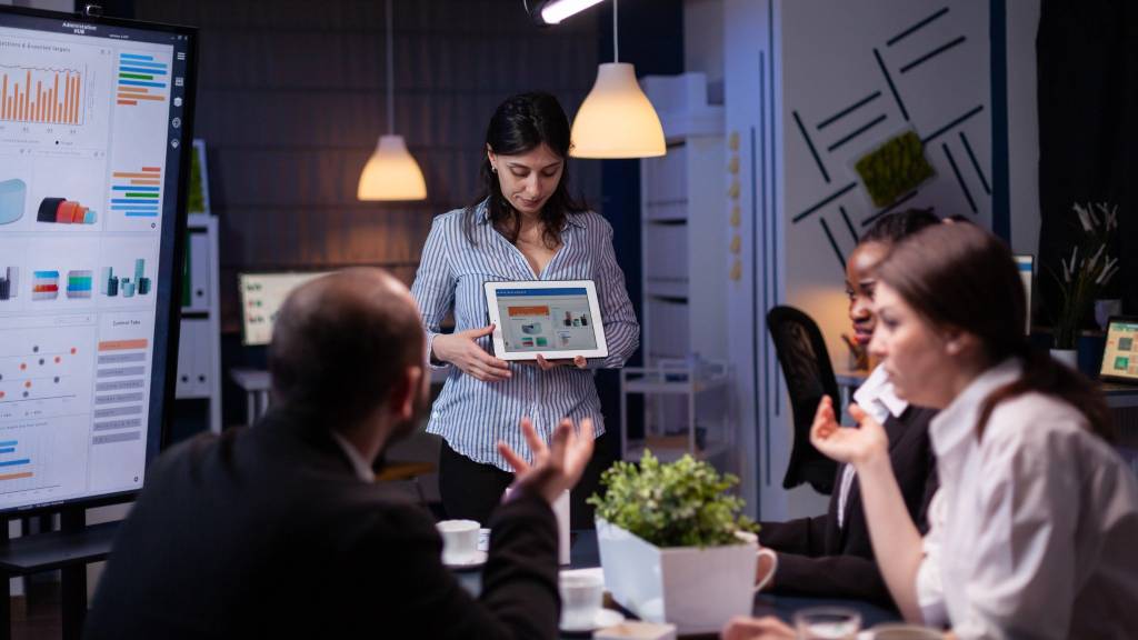 Marketing professional presenting analytics dashboard on a tablet during a digital marketing meeting focused on AI-driven strategies.