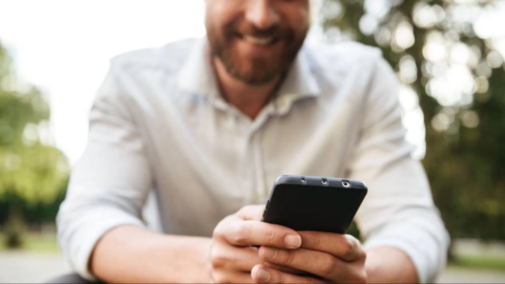 A smiling professional using a smartphone outdoors to interact on social media, illustrating personalized engagement and digital marketing trends in 2025.