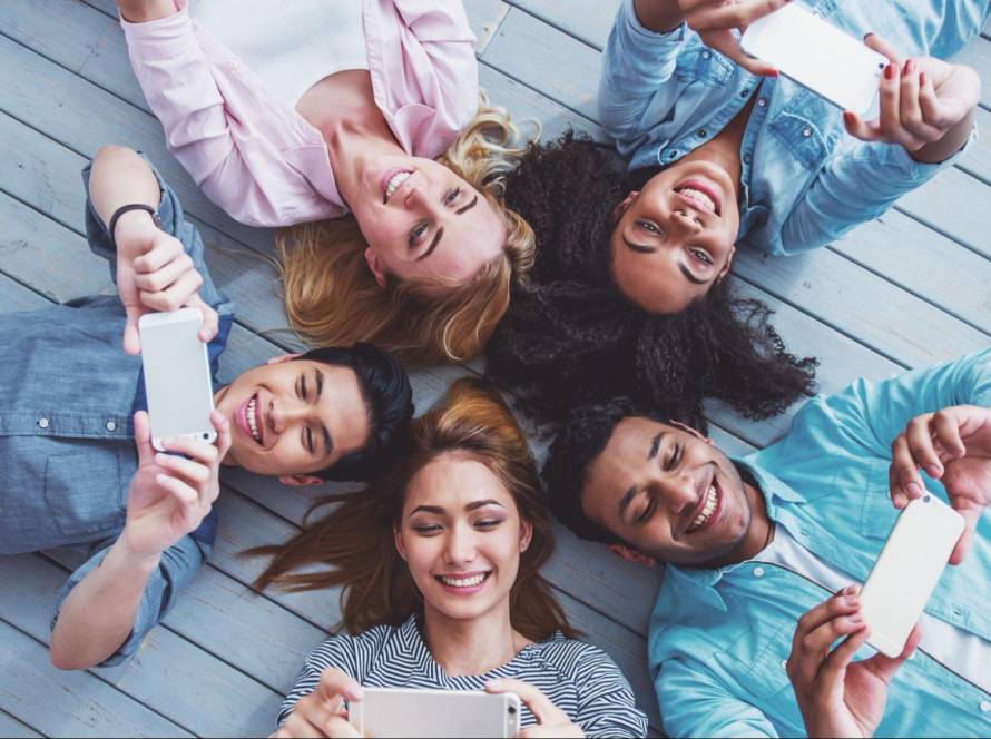 A group of friends lying on the floor using smartphones to create and share social media posts, symbolizing engagement and connection on Instagram in 2025.