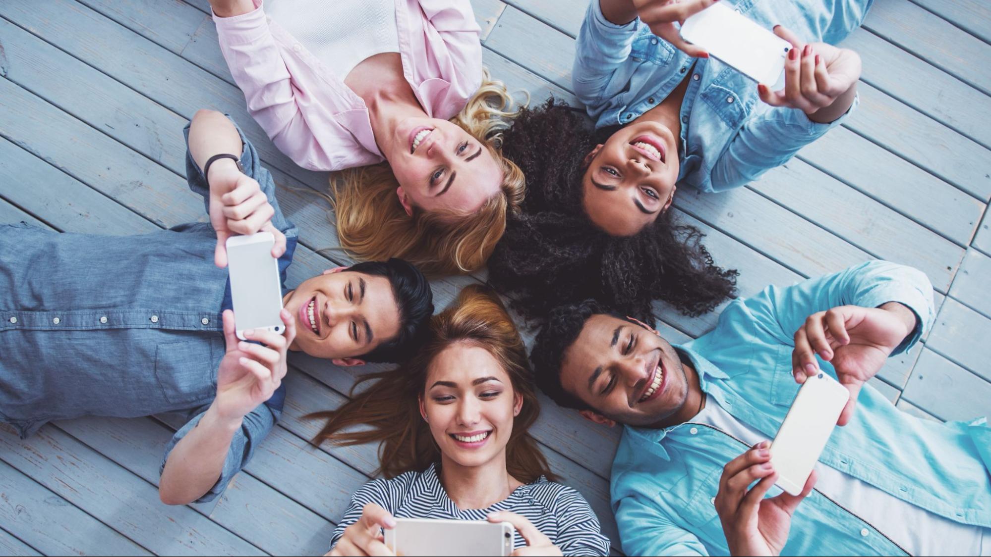 A group of friends lying on the floor using smartphones to create and share social media posts, symbolizing engagement and connection on Instagram in 2025.