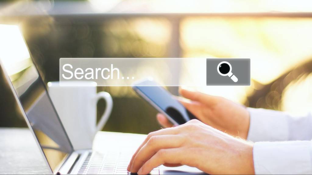 Person using a smartphone and laptop to search online, representing how SEO and AI in 2026 influence business discovery and leads.