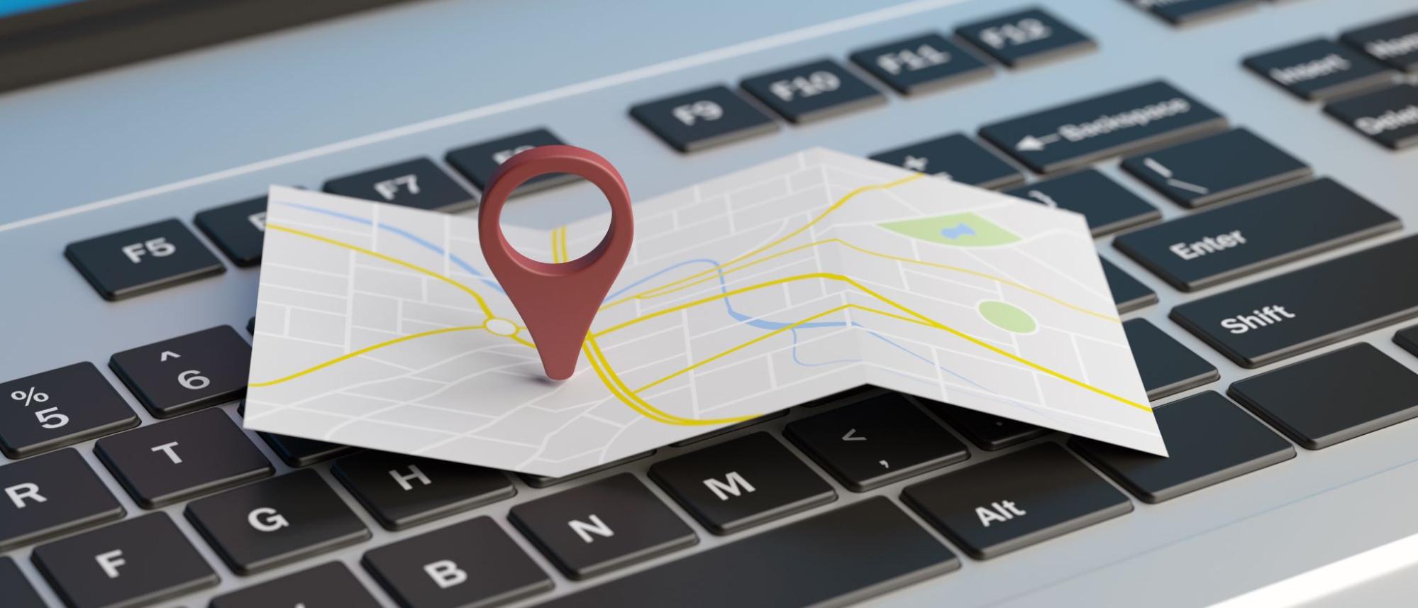 A 3D illustration of a red map pointer on a folded map resting on a laptop keyboard, symbolizing how the Google Maps AI update helps local businesses gain digital visibility.