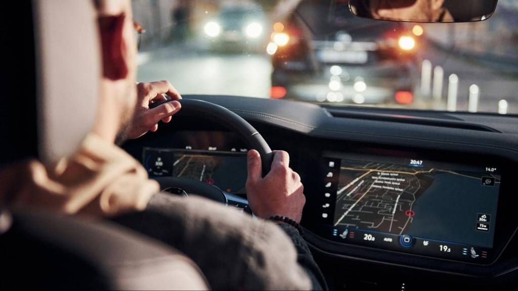 A man driving a modern vehicle using a large dashboard screen displaying the new Google Maps immersive navigation, highlighting the AI-driven 3D map experience for users.