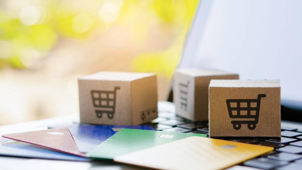 Small cardboard boxes with shopping cart icons and colorful credit cards resting on a laptop, illustrating the incentivized review practices like gift cards and discounts that Google is now penalizing.
