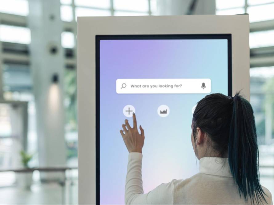 A woman interacting with a digital touch screen featuring an AI-powered search engine with voice and text search capabilities.
