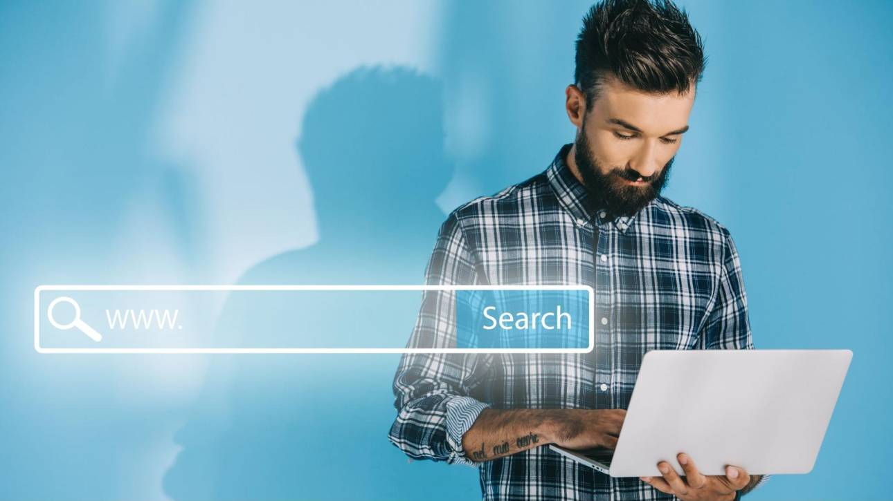A man typing on a laptop next to a glowing web search bar graphic, representing the process of finding your perfect AI assistant.
